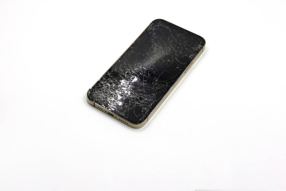 A gold iPhone with a cracked screen on a clean white surface